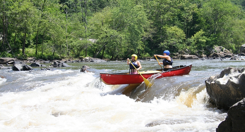 Two people wearing safety gear paddle a canoe through whitewater 